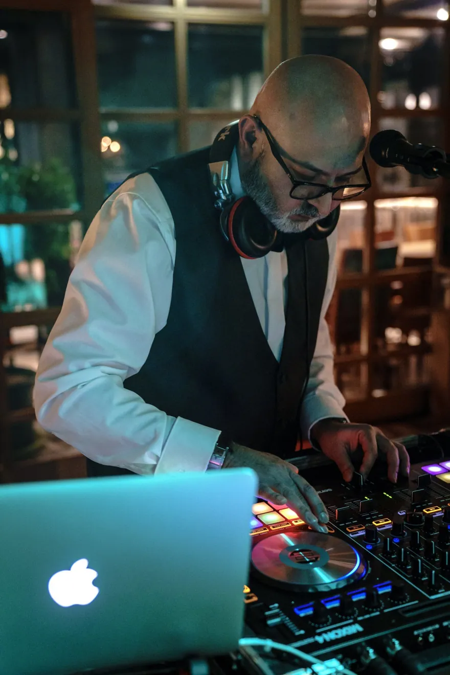 Chico mit Weste und Kopfhörern konzentriert am beleuchteten DJ-Pult