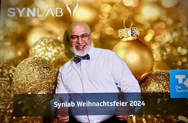 Chico vor einer goldenen Fotowand bei der Synlab-Weihnachtsfeier 2024