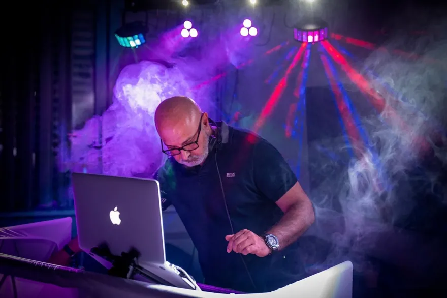 Chico am Laptop und DJ-Pult vor farbigen Lichtstrahlen im Nebel