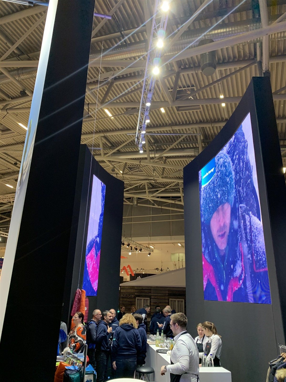 Messestand mit hohen digitalen Displays und Gästen beim Get-together
